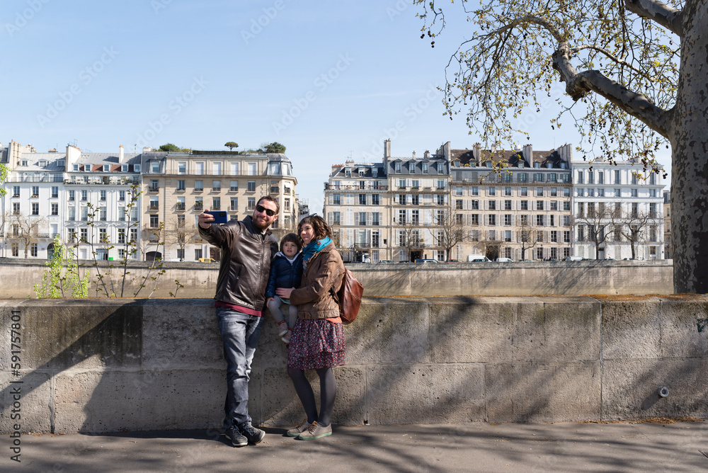 Family with one little girl taking a selfie with beautiful Parisian buildings on the background during her vacations in Paris.