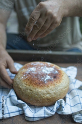 Baker's hand sprinkles flour on fresh bread close-up. A man finishes baking, decorates warm bread. Traditional village recipe, home baking concept
