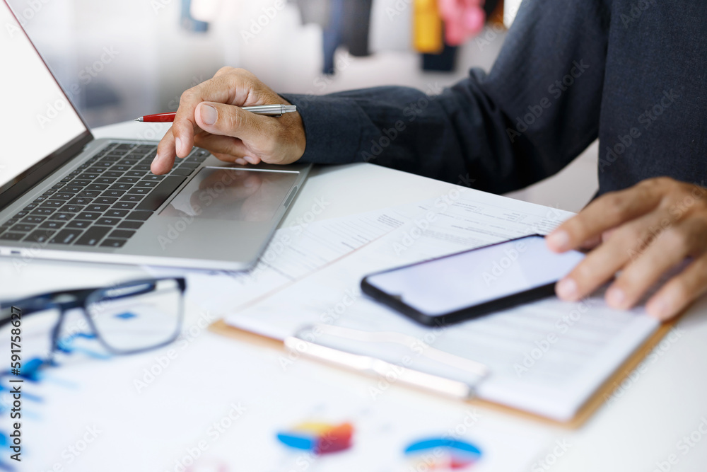Asian businessman using laptop computer and smart phone contact business search information on desk at home office advising clients on investment planning Asian businessman using laptop computer and smart phone contact business search information on desk at home office advising clients on investment planning