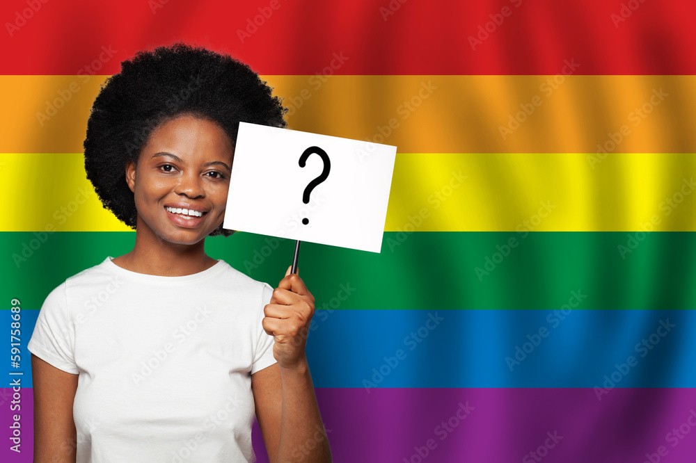 Happy smiling african american woman holding sign with question mark on it on LGBT flag background Happy smiling african american woman holding sign with question mark on it on LGBT flag background