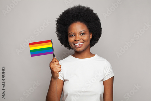 Portrait of happy smiling african american woman holding LGBT flag on grey background