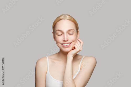 Portrait of gorgeous woman touching her cheek and laughing isolated on grey background. Beauty  cosmetics  skincare  glamour