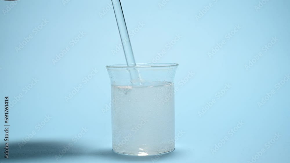 Close-up using glass stick for stirring a fizzy solution with bubbles after dissolving a pharmaceutical therapeutic effervescent tablet, over isolated blue background. Dissolution of medical pill Close-up using glass stick for stirring a fizzy solution with bubbles after dissolving a pharmaceutical therapeutic effervescent tablet, over isolated blue background. Dissolution of medical pill
