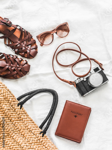 Women's accessories for summer holidays, travel - passport, sunglasses, camera, leather sandals and straw bag on a white background, top view