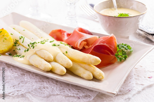 Traditional German white asparagus with air dried Parma ham and tomatoes served as close-up on a design plate