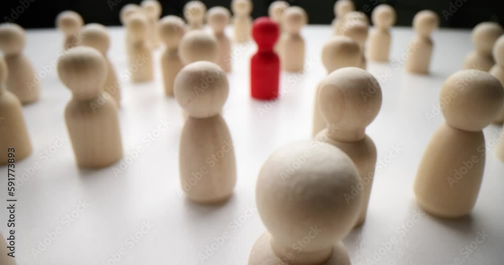 Red human figure surrounded by white wooden figurines standing out of crowd on white table surface. Leadership and nonconformity concept Red human figure surrounded by white wooden figurines standing out of crowd on white table surface. Leadership and nonconformity concept