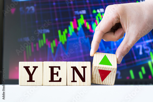 A hand rotates a wooden cube to indicate the fall or rise of the Yen