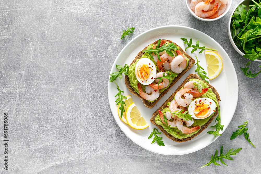 Toast with shrimps, avocado guacamole, arugula and boiled egg, top view