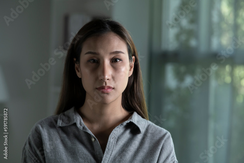 Portrait of sad and worried young Asian woman in living room, looking at camera