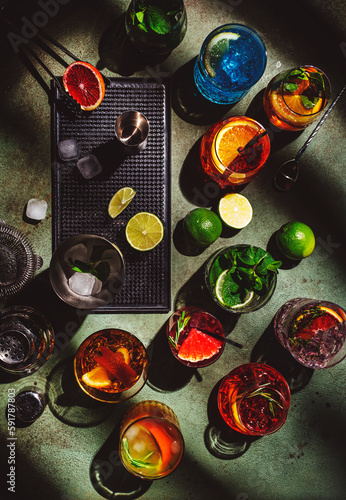 Cocktails set on rusty green bar counter, top view. Mixology concept. Assortment of colorful strong and low alcohol drinks for summer cocktail party. Dark background, bar tools, hard light, top view