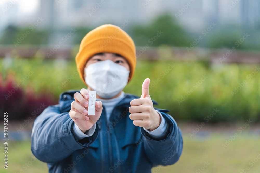 Asian man wearing a mask is holding a negative self-test antigen result. Asian man wearing a mask is holding a negative self-test antigen result.