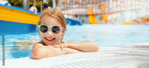 happy little girl with sunglasses in swimming pool at outdoor water park on sunny summer day. banner with copy space