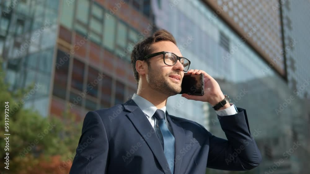 Phone. Man talking on mobile phone in city business district. Confident young businessman having a smartphone conversation smiling happy wearing suit and eyeglasses outdoors. Male professional in 30s Phone. Man talking on mobile phone in city business district. Confident young businessman having a smartphone conversation smiling happy wearing suit and eyeglasses outdoors. Male professional in 30s