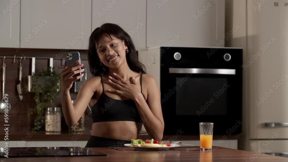 Smiling black girl shows her breakfast to camera during video call in her kitchen Smiling black girl shows her breakfast to camera during video call in her kitchen