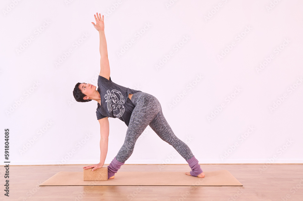 Naklejka premium A young woman performing the Warrior pose, Virabhadrasana, using a cork yoga block for support.