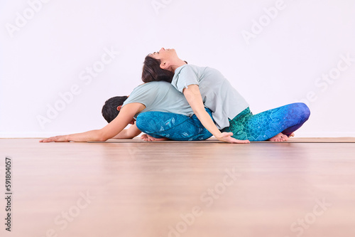 Two girls doing yoga, one performing Paschimottanasana pose and the other letting her back fall on top