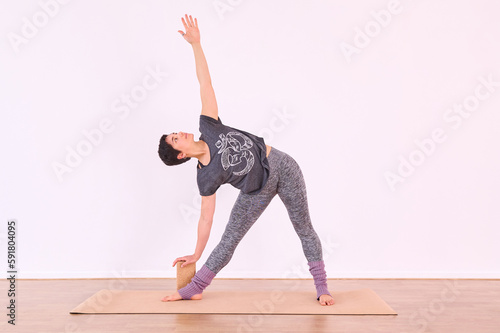 A female practitioner doing the Virabhadrasana or Warrior pose with the assistance of a cork yoga block.