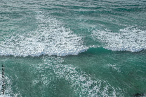 Ocean foamy waves approaching rocky shore. Top view.