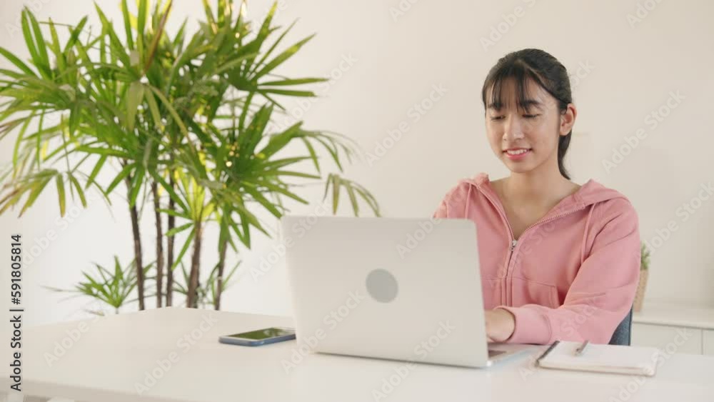 Young Asian woman sitting on laptop, working, playing social media indoor in the morning.Teenager women Asian chatting with friend happy smiling Young Asian woman sitting on laptop, working, playing social media indoor in the morning.Teenager women Asian chatting with friend happy smiling