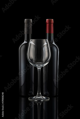 Two wine bottles next to each other, a wine glass in front of a black background