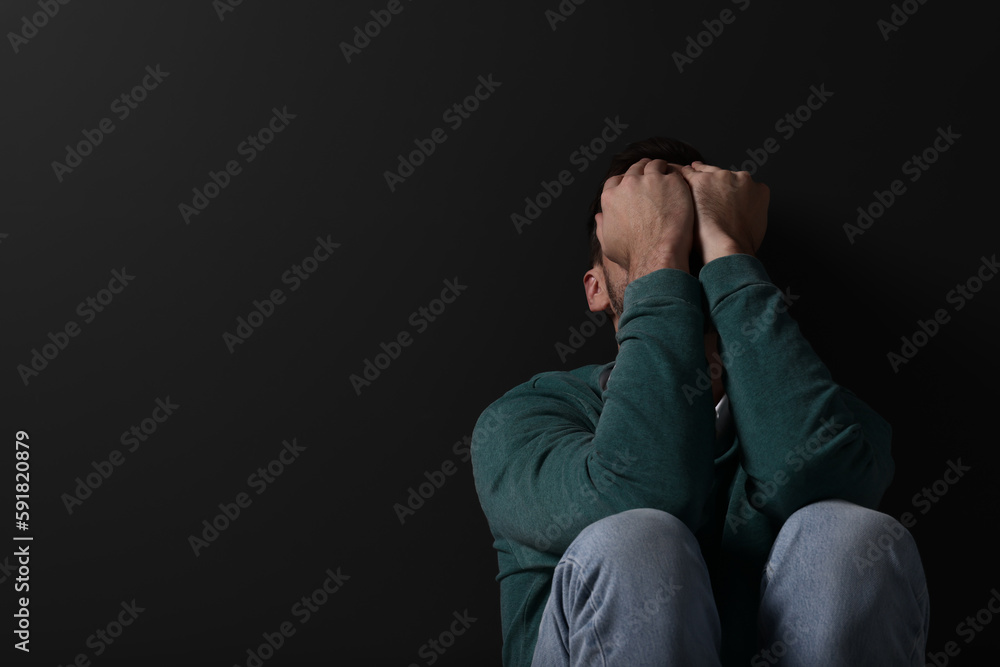 Upset man sitting on black background. Space for text Upset man sitting on black background. Space for text