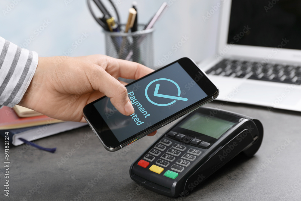 Woman using terminal for contactless payment with smartphone at office table, closeup. Transaction completed screen on device Woman using terminal for contactless payment with smartphone at office table, closeup. Transaction completed screen on device