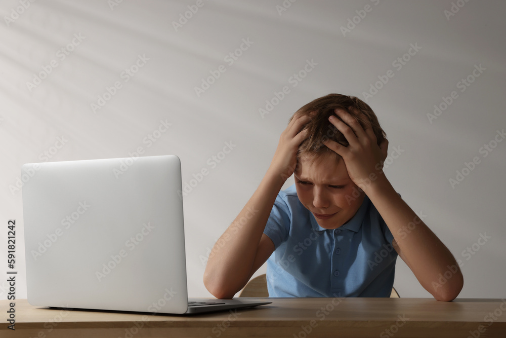 Upset boy with laptop at wooden table. Cyber bullying Upset boy with laptop at wooden table. Cyber bullying