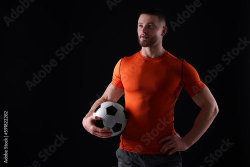 Athletic young man with soccer ball on black background. Space for text