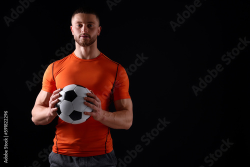 Athletic young man with soccer ball on black background. Space for text