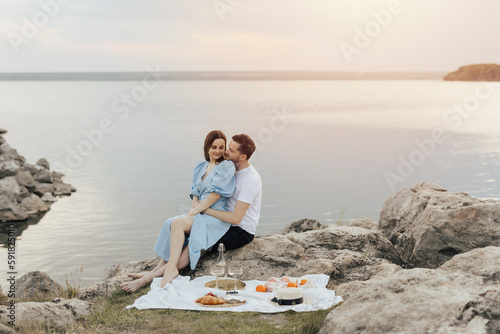 Summer picnic on the beach. Beautiful young couple flirting and enjoying a company of each other on a romantic picnic.