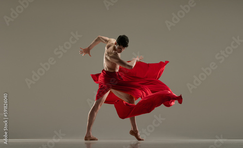 Classic and modern ballet. Artistic, handsome young man, dancer performing with red silk fabric against grey studio background. Concept of art, classical dance, inspiration, creativity, choreography