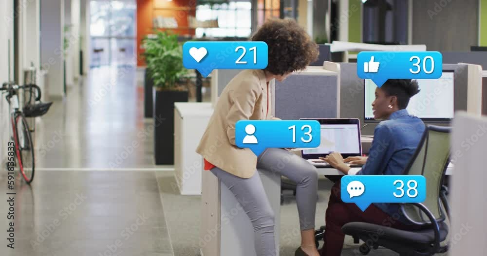 Animation of social media icons with numbers over diverse business people using laptop at office Animation of social media icons with numbers over diverse business people using laptop at office