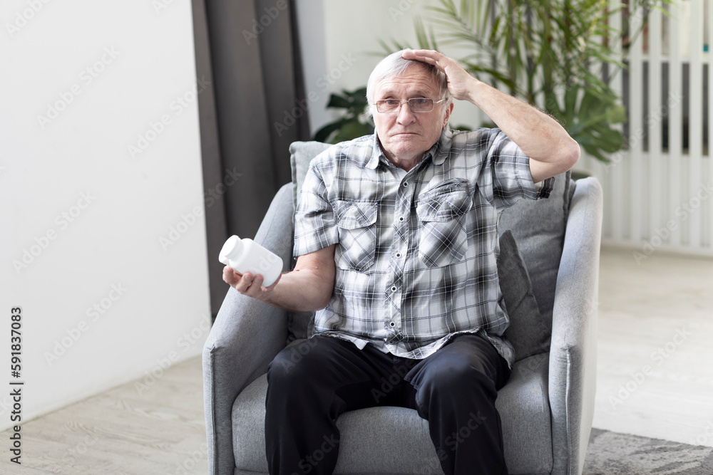 Confused aged man sits on the armchair and holds can with medicine and forgets what to do Confused aged man sits on the armchair and holds can with medicine and forgets what to do