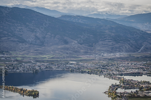 Bird's eye view of a town on the shore of a lake against a mountain range on a cloudy day