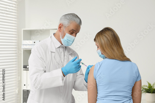 Doctor giving hepatitis vaccine to patient in clinic  back view