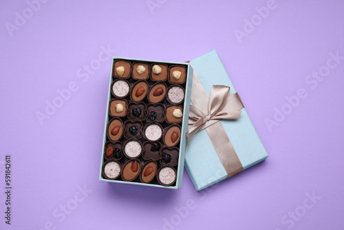 Open box of delicious chocolate candies on violet background, top view