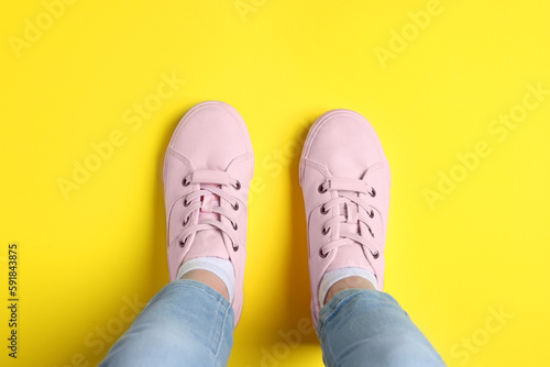 Woman in stylish sneakers standing on yellow background, top view
