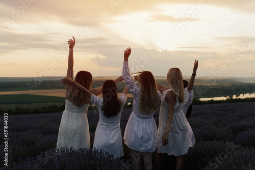 Five best girlfriends having fun together on a picnic on the lavender field at sunset. They enjoying time in nature at weekend. Copy space.