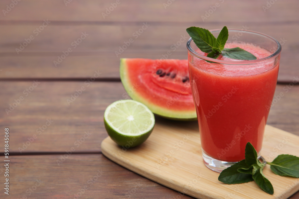 Glass of delicious watermelon smoothie with mint and fresh cut fruits on wooden table. Space for text Glass of delicious watermelon smoothie with mint and fresh cut fruits on wooden table. Space for text