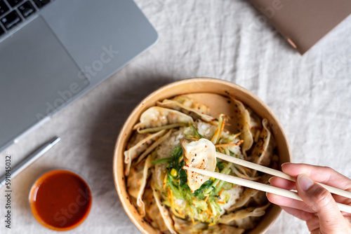 Asian takeaway food box with rice and dumplings on the office desk near the laptop.