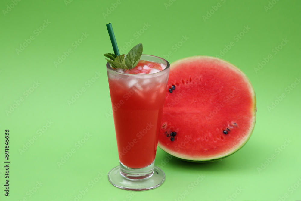 Glass of delicious drink with mint, ice cubes and cut fresh watermelon on light green background Glass of delicious drink with mint, ice cubes and cut fresh watermelon on light green background