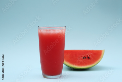 Glass of delicious drink with ice cubes and cut fresh watermelon on light blue background