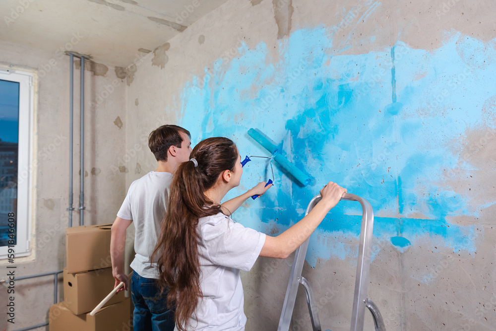 Foto de Couple in new home during repair works painting wall together. Happy family holding