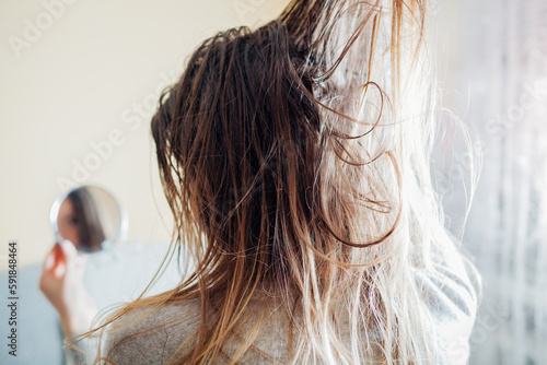 Close up of woman touching dirty oily and greasy hair looking in mirror at home. Time to wash head with shampoo photo