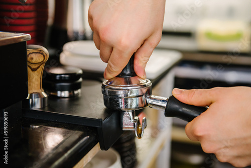 A barista in a cafe presses coffee into a holder and prepares to brew coffee.