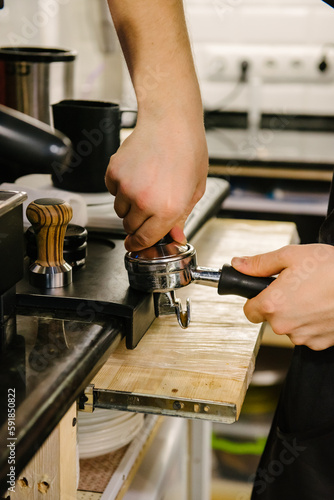 A barista in a cafe presses coffee into a holder and prepares to brew coffee.