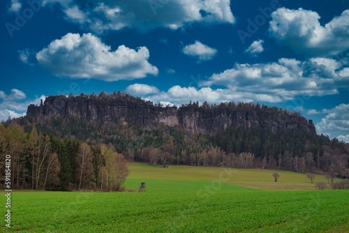 Scenic view of an agricultural field, trees and a huge cliff under the cloudy sky
