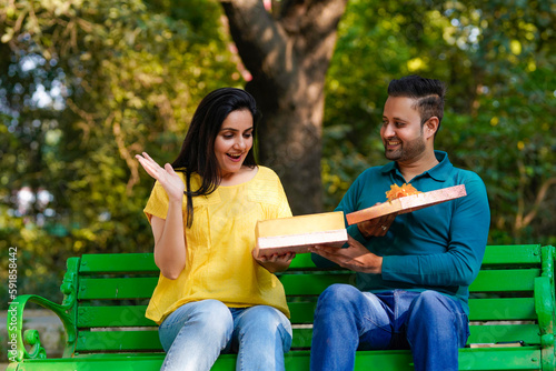 Young man giving surprise gift to young woman at park. © PRASANNAPIX