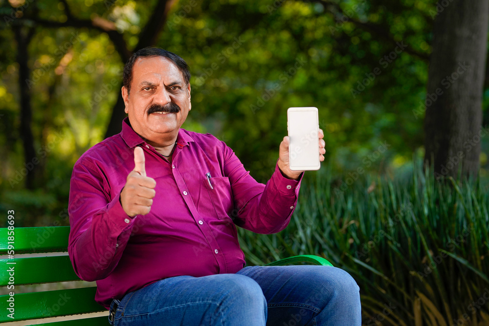 Indian man showing smartphone screen with thumps up at park. Indian man showing smartphone screen with thumps up at park.
