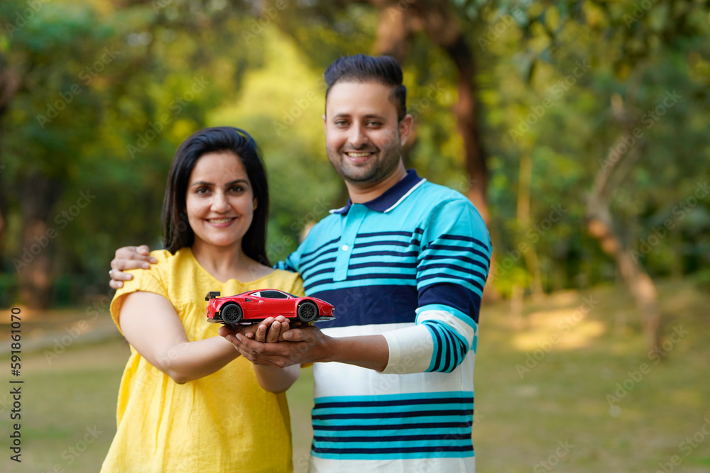 Young indian couple holding car toy in hand and giving expression at park. Young indian couple holding car toy in hand and giving expression at park.